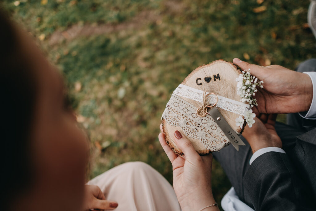 Zwei Ringe, auf einer Holzscheibe werden zwischen zwei Menschen weitergereicht.