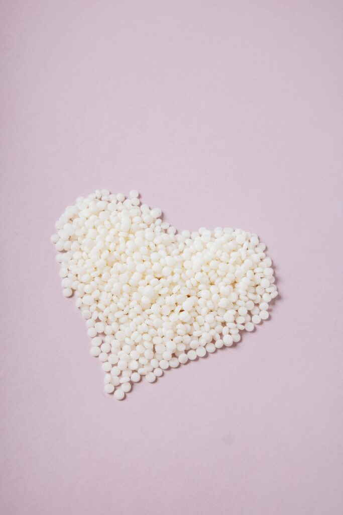 Weiße Wachsperlen zu einem Herzen geformt auf rosa Hintergrund.